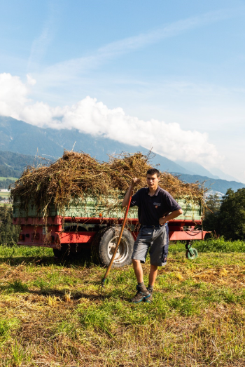 Jugendlicher bei der landwirtschaftlichen Arbeit vor Bergpanorama und blauen Himmel
