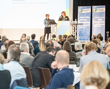 Ein voller Saal, vorne einen Bühne mit Präsenatitonen.