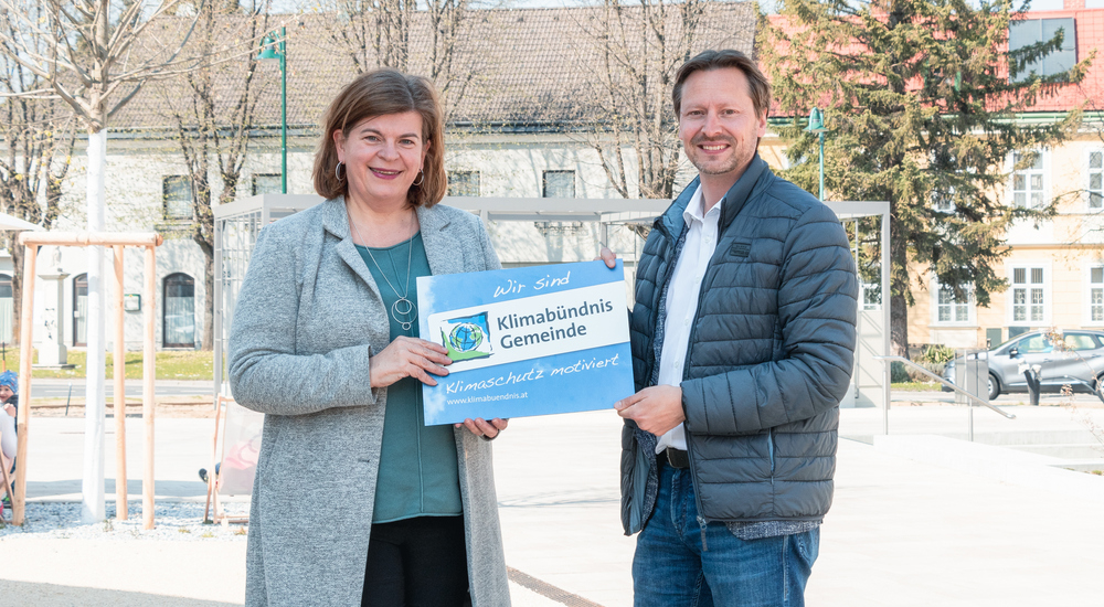 Petra Schön und Rainer Handflinger mit der Klimabündis-Tafel am Gemeindeplatz.
