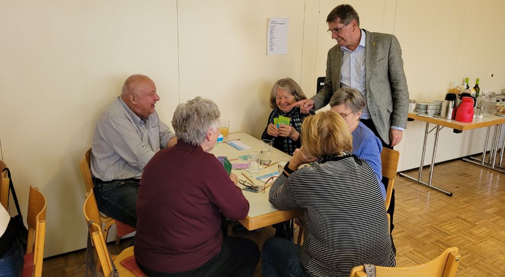 4 Personen sitzen an einem Tisch, Bürgermeister Gosch steht daneben und deutet auf den Tisch.