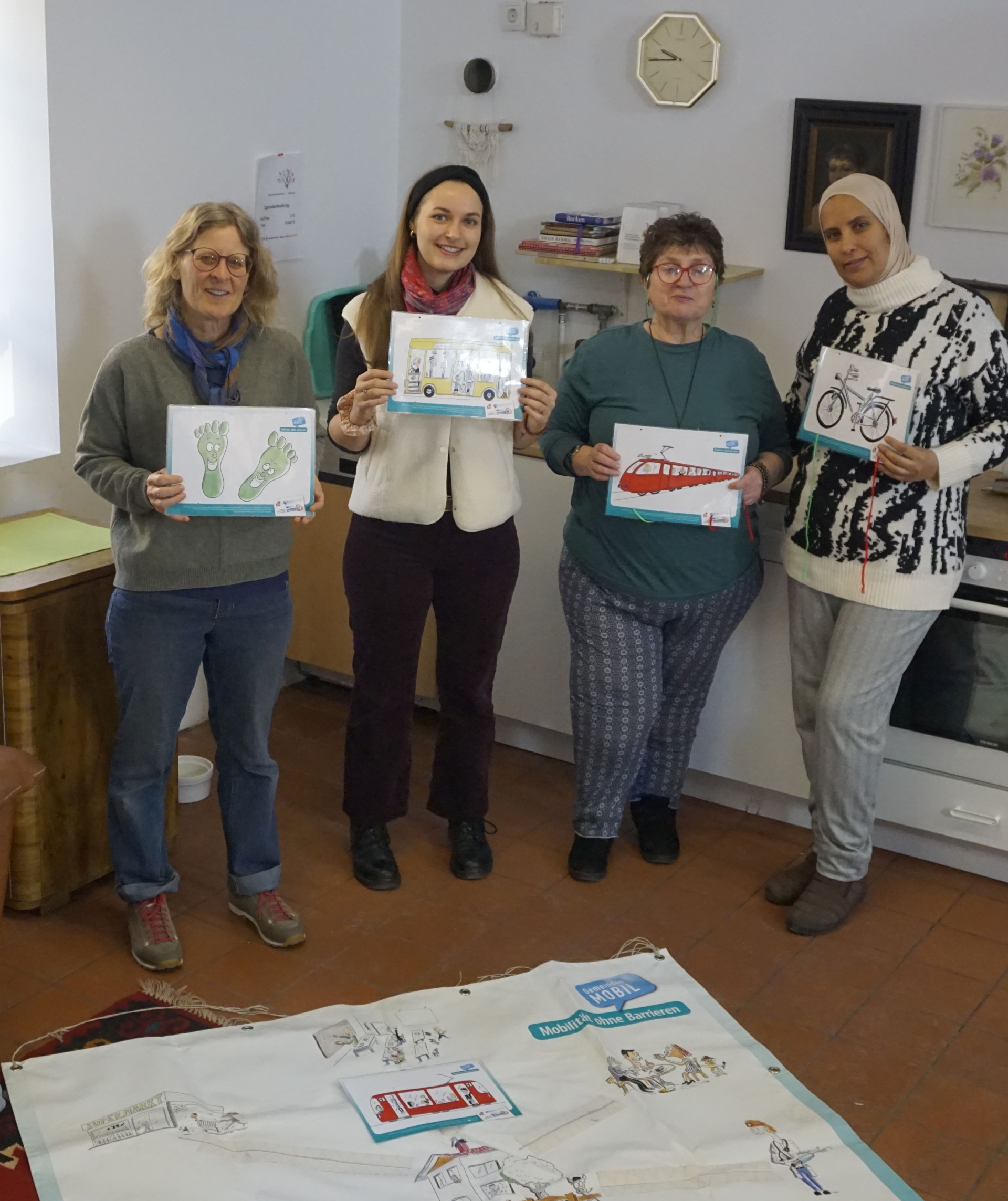 Vier Frauen mit Bildern von Verkehrsmitteln in der Hand stehen vor Plakat, das am Boden liegt