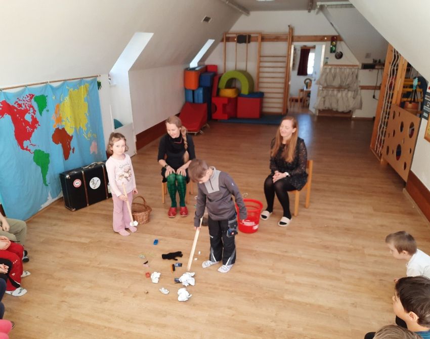 Kinder heben in einem Raum Müll auf mit einer Zange