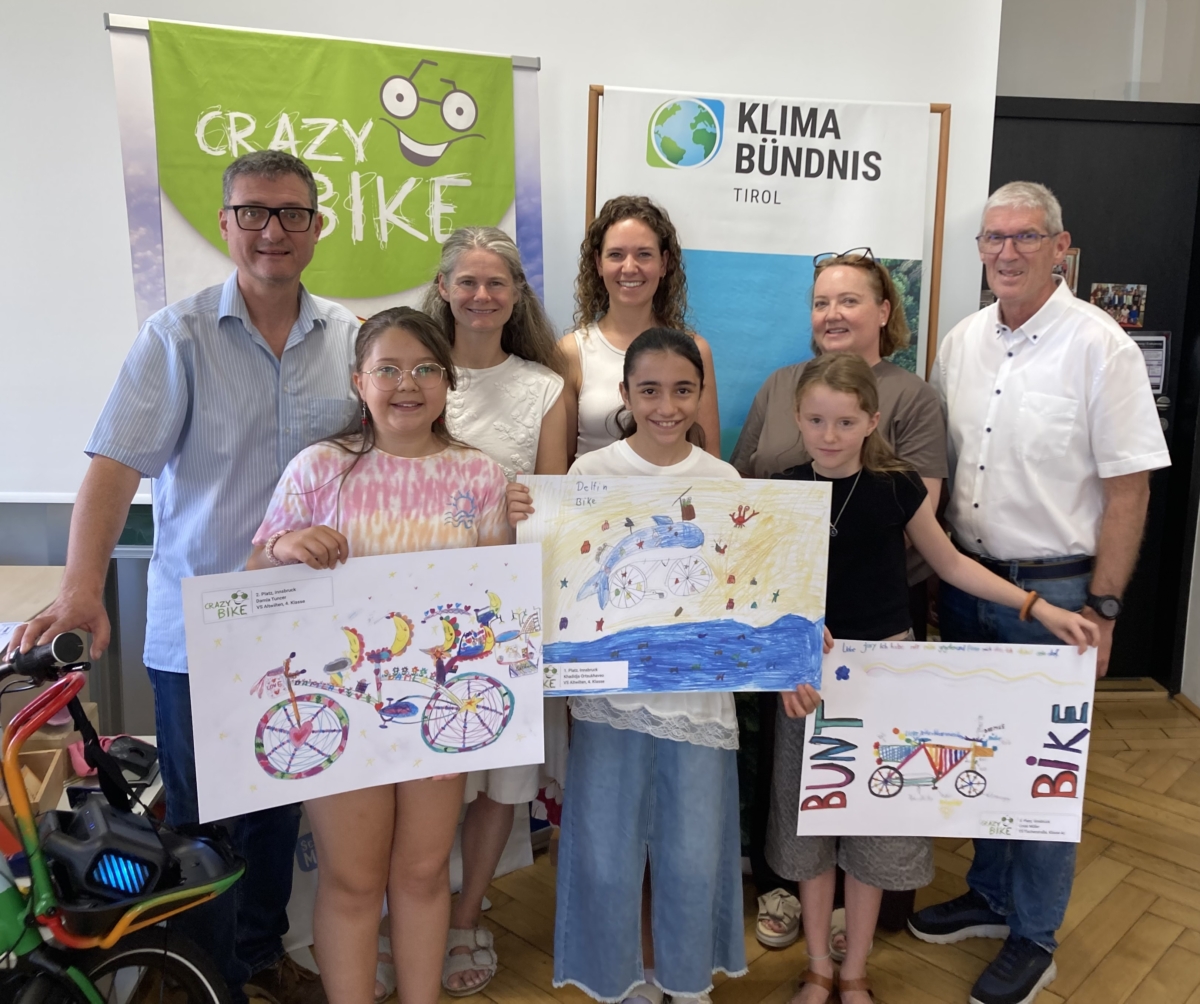 in buntes Fahrrad, drei Kinder stehend mit Zeichnungen von Fahrrädern und drei Erwachsene im Hintergrund in einer Schulklasse